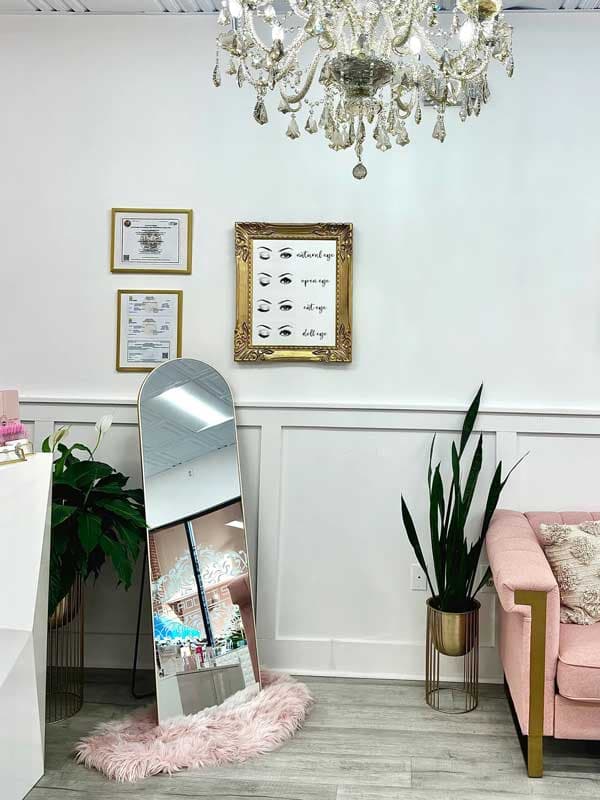 The Lash Addict Studio Seminole waiting area, with a crystal chandelier, framed eye-shape diagrams, and a pink velvet couch.