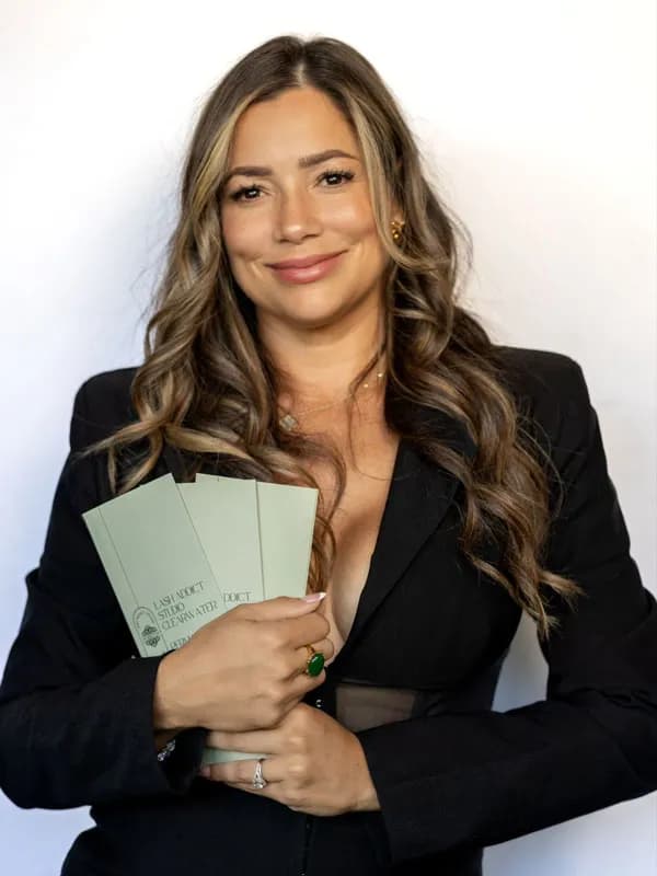 Portrait of Natali, founder of Lash Addict Studio, in a black blazer holding a fan of studio cards.