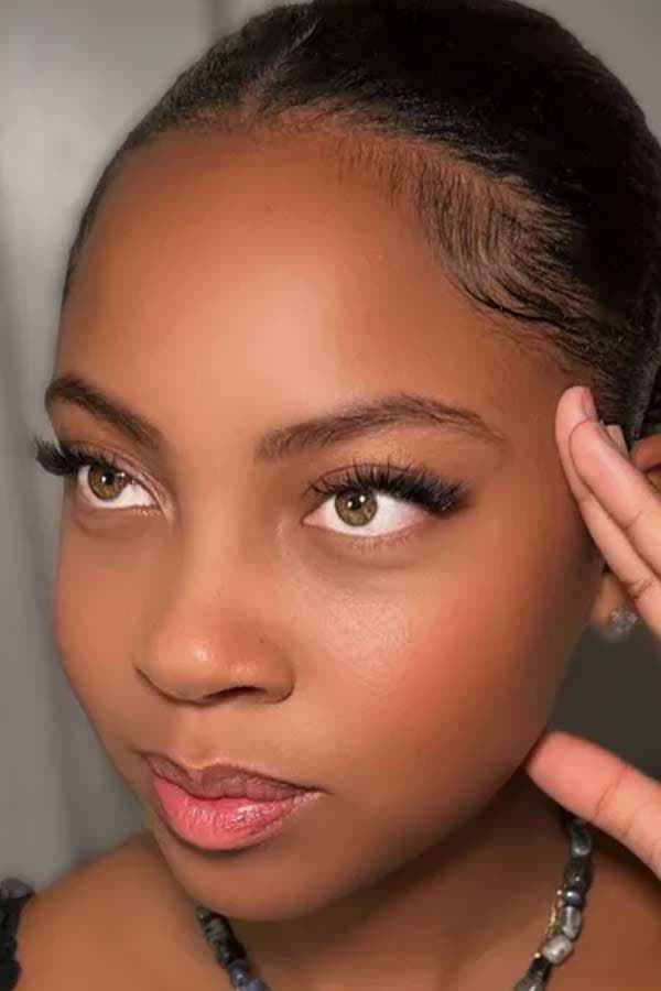Close-up portrait of a client with lash extensions, hand resting near her temple.