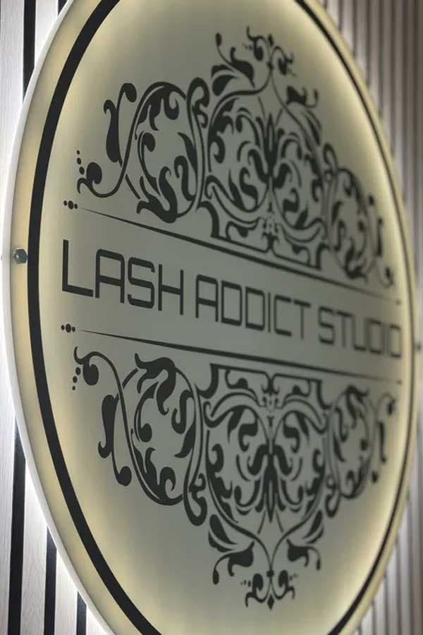 Close-up of the illuminated, ornately framed Lash Addict Studio wall sign.